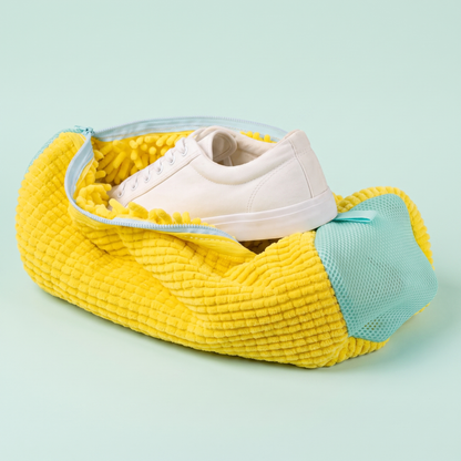 Sac de lavage jaune à microfibres, fermeture turquoise et basket blanche sur fond menthe