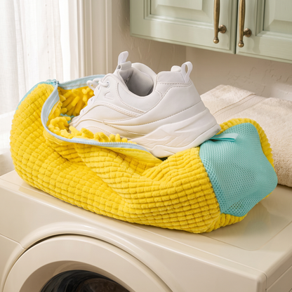 Sac de lavage jaune et basket blanche sur une machine à laver dans une buanderie aux tons crème et sauge
